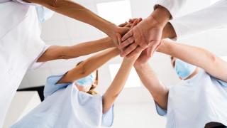 Terveydenhuollon ammattilaiset seisovat ryhmänä kädet yhdessä