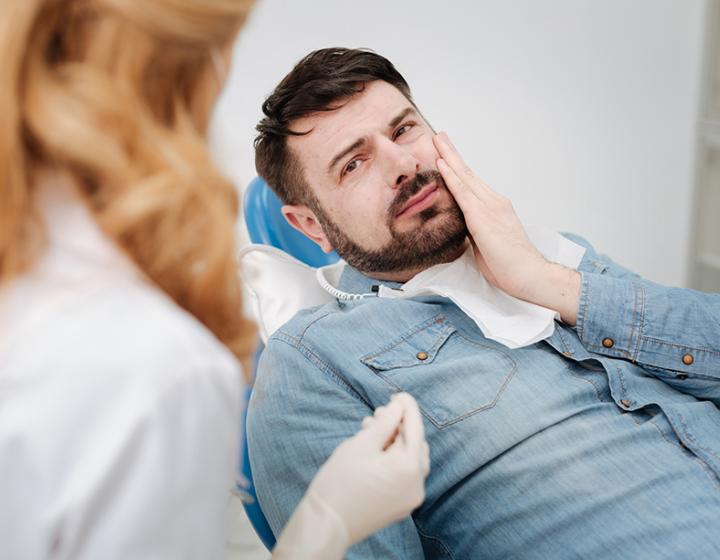 Hammassärystä kärsivä miespotilas pitelee poskeaan hammaslääkärin vastaanotolla